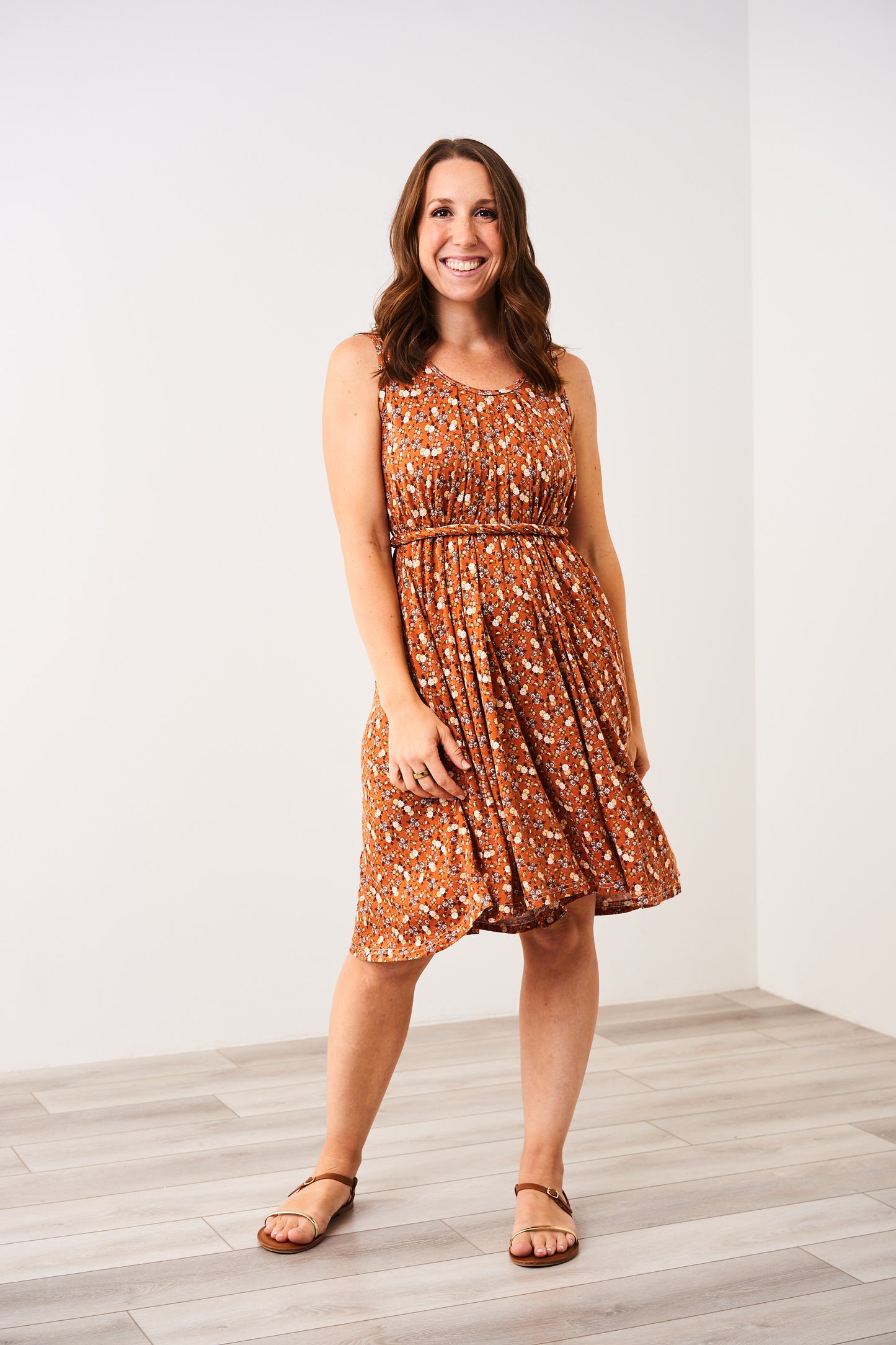 Woman wearing an orange and white patterned floral Latched Mama nursing romper standing against a white wall.