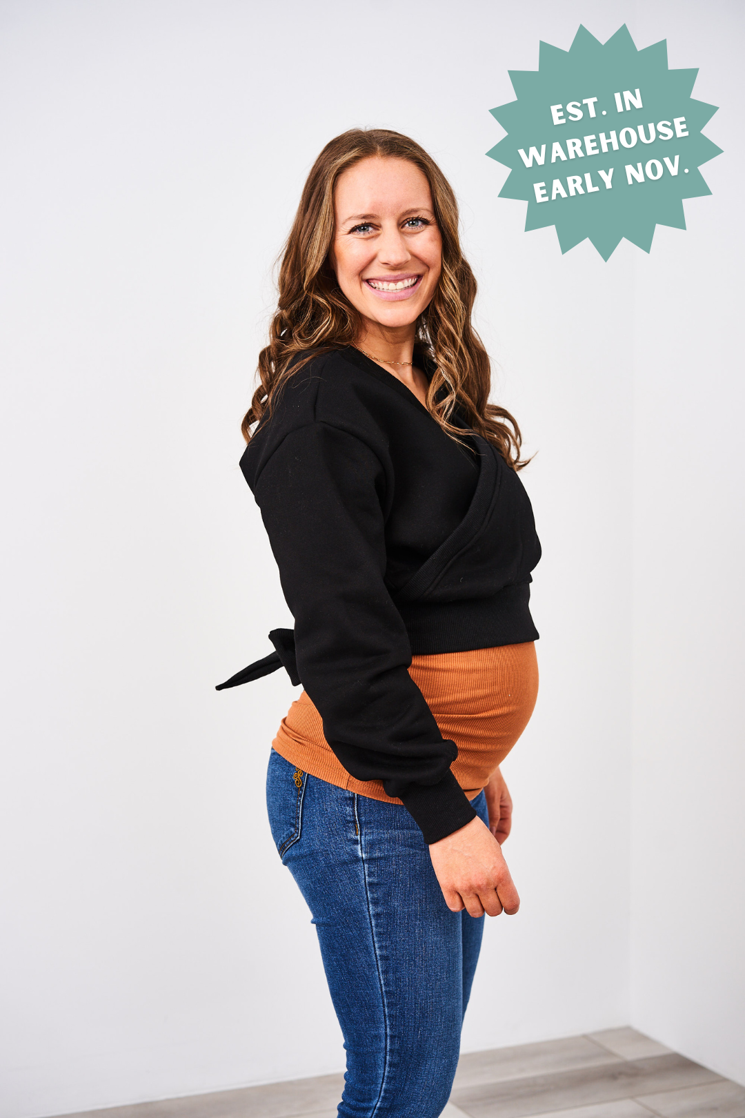 Woman wearing a black sweater over a brown top with text 'EST. IN WAREHOUSE EARLY NOV.'