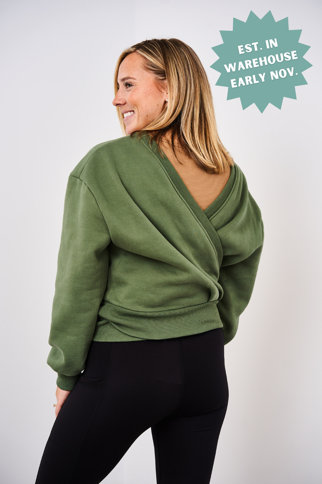 Woman wearing a green sweater with a back design, standing against a white background.