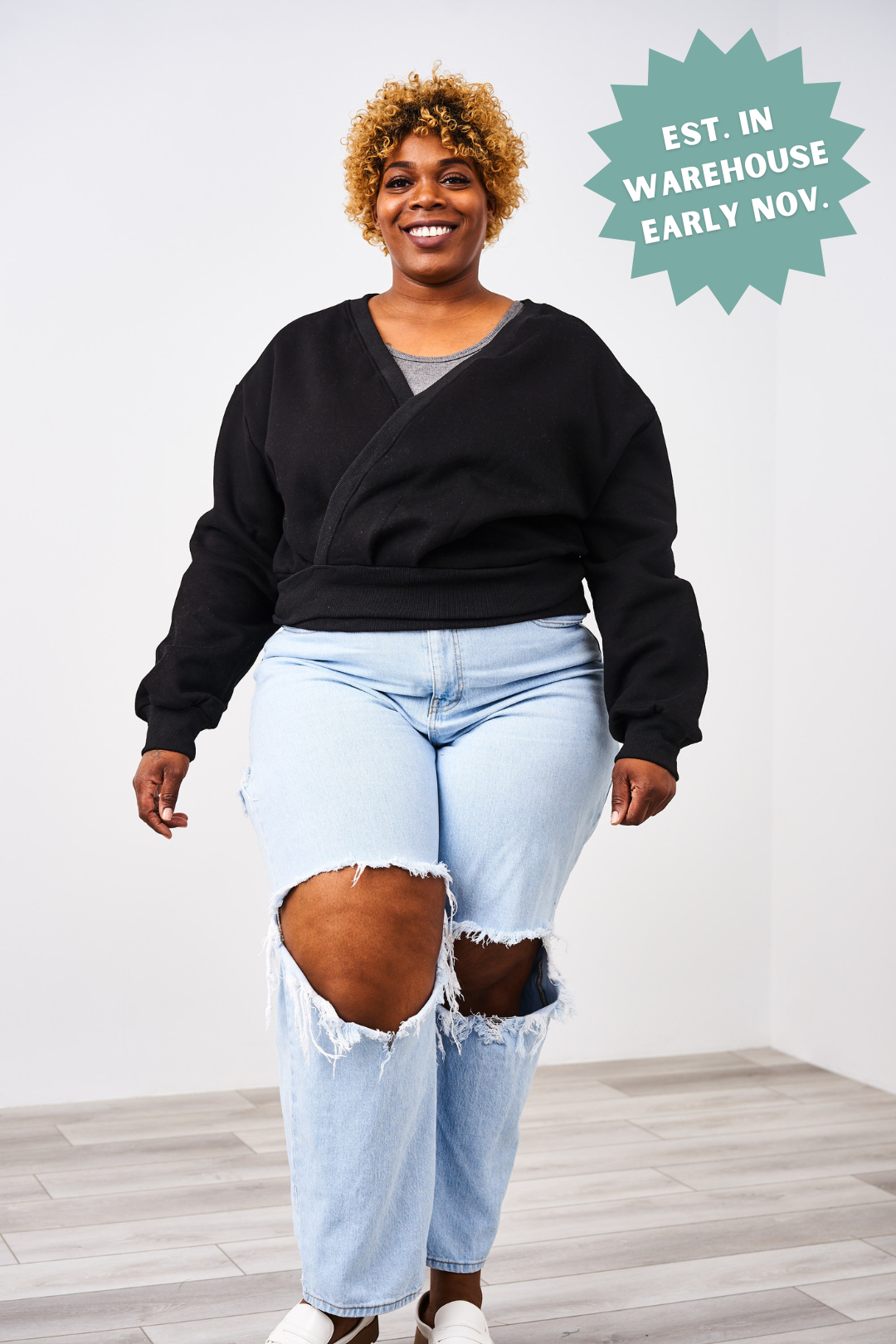 Person wearing a black sweater and light blue ripped jeans with a white background