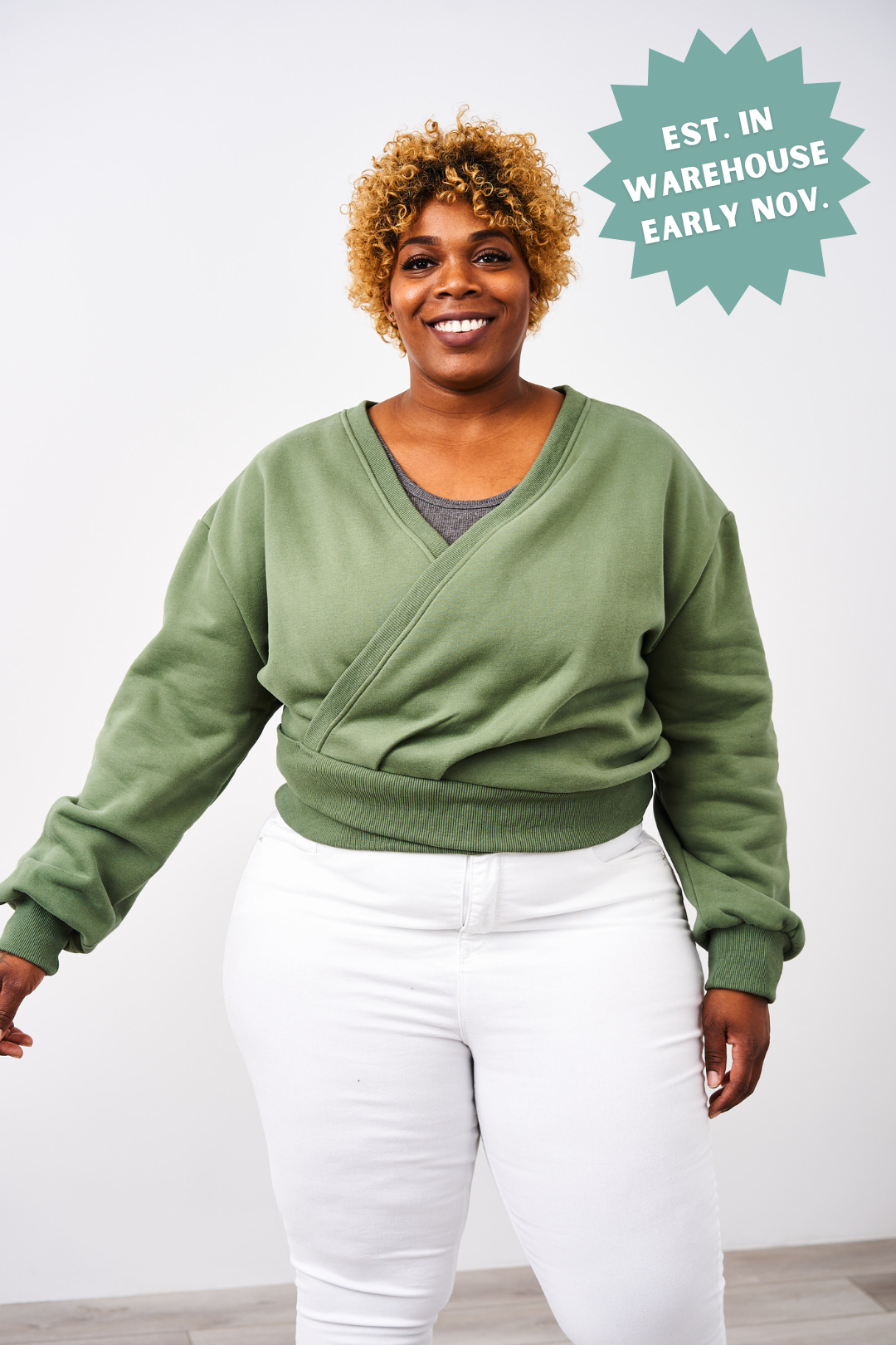 Woman wearing a green sweater and white pants with a white background