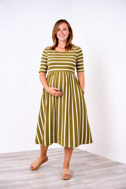 Pregnant woman wearing a green and white striped Latched Mama nursing dress standing against a white background