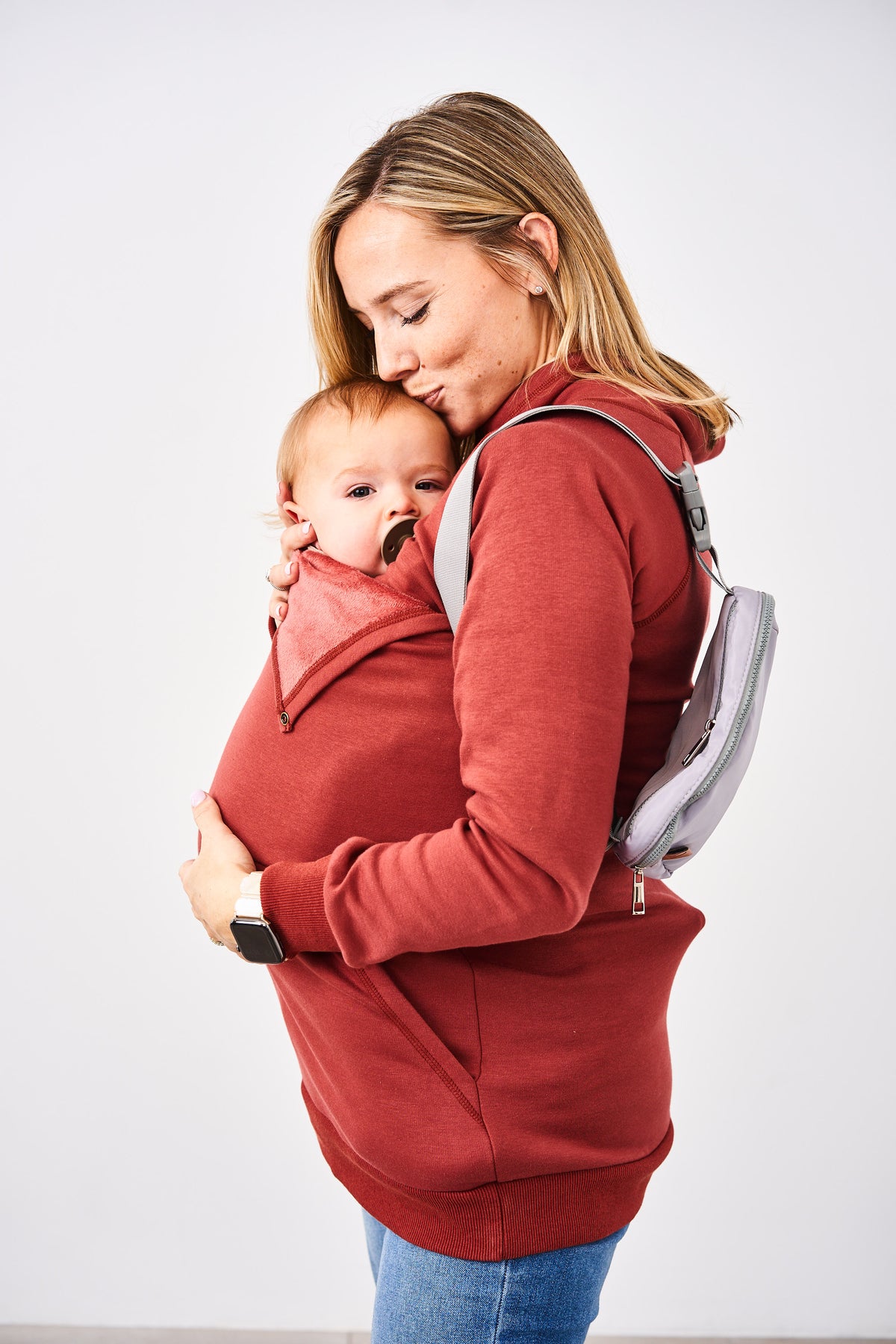 Woman wearing a Latched Mama Rust Harbor Snap Nursing Pullover over a baby carrier with a baby inside, against a white background
