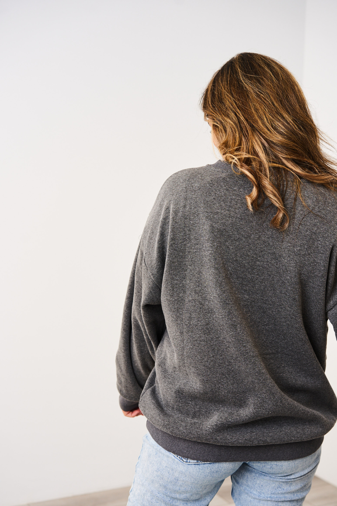 Person wearing a Charcoal Latched Mama 635 Snuggle Up Nursing Pullover and light blue jeans against a white background