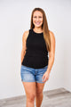 A woman wearing a Latched Mama high neck ribbed nursing tank top in black with blue denim shorts.