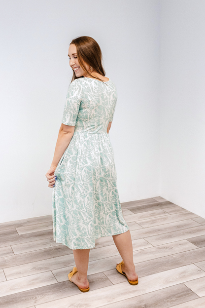 Woman showing the back of the latched mama classic cotton nursing dress in aqua drift, which is a light sage green color.