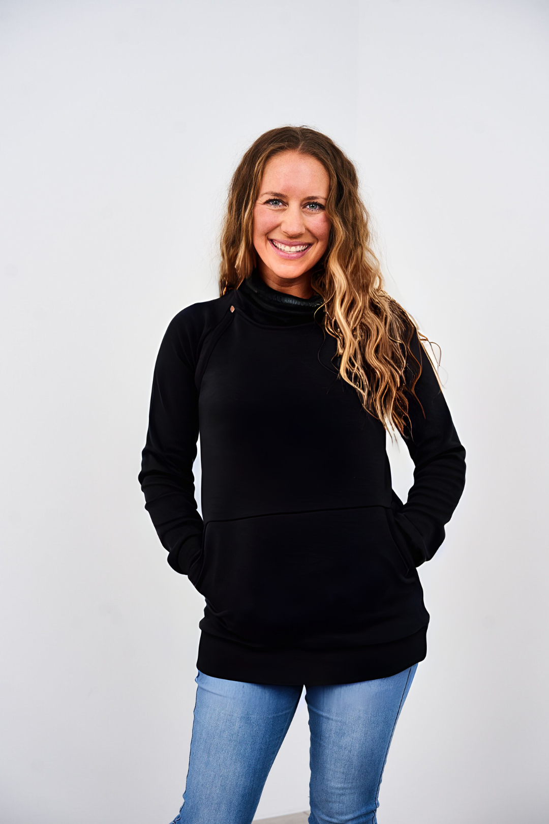Woman wearing a black Latched Mama Harbor Snap Nursing Pullover and blue jeans against a white background