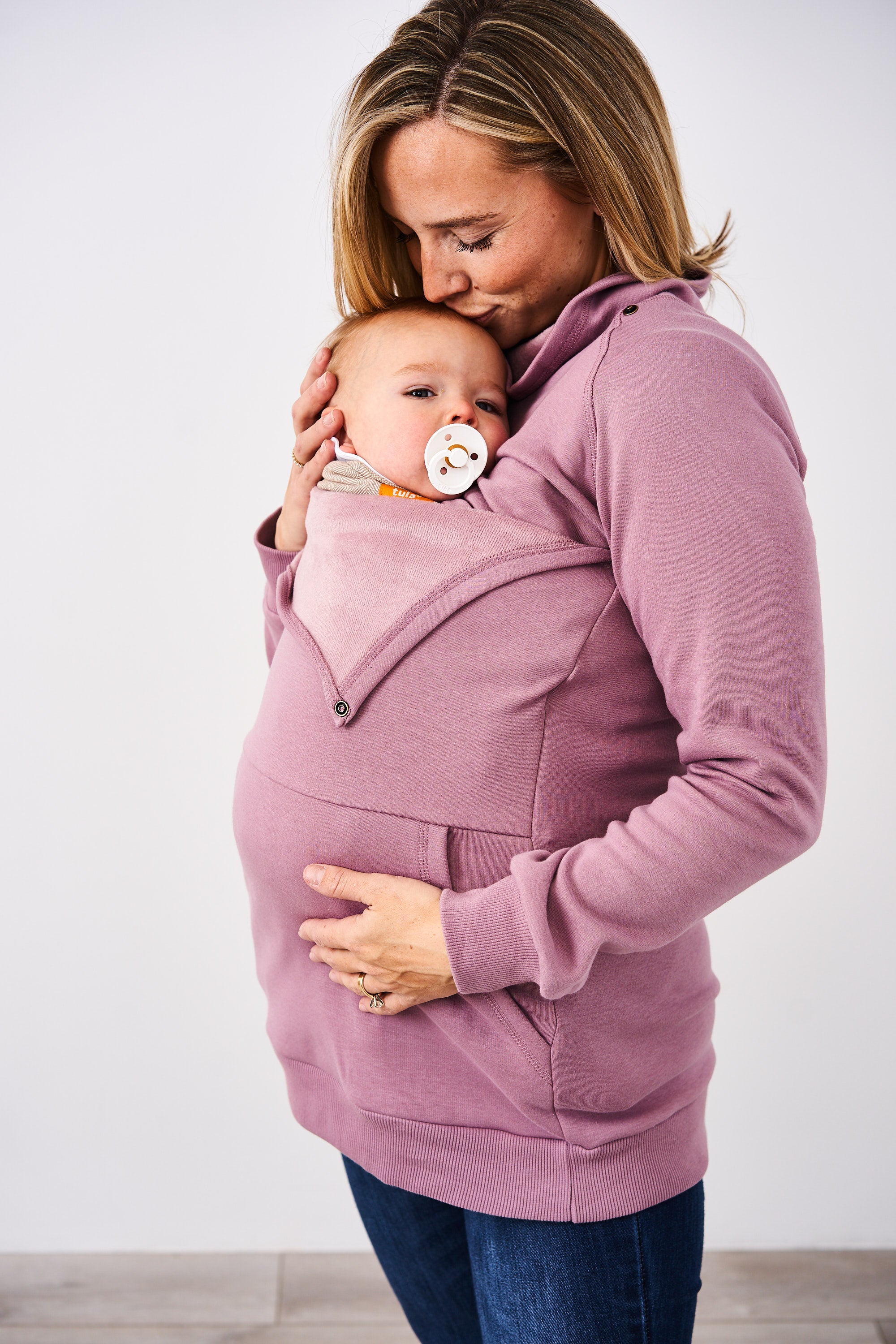Woman wearing a Latched Mama Lavender Harbor Snap Nursing Pullover over a baby carrier against a white background