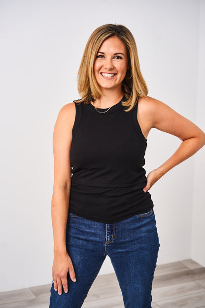 Woman wearing a black Latched Mama nursing ribbed tank top and blue jeans against a white background.