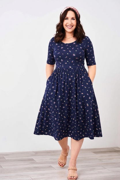 Woman wearing a Latched Mama nursing navy blue dress with a subtle pattern on a white background
