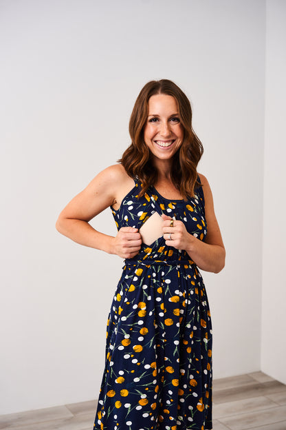 Woman wearing the Latched Mama Momper dandelion print sleeveless nursing romper against a white background