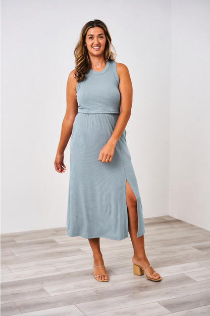 Woman wearing the Latched Mama ribbed midi slit nursing dress in dusty blue with heels on a white background.