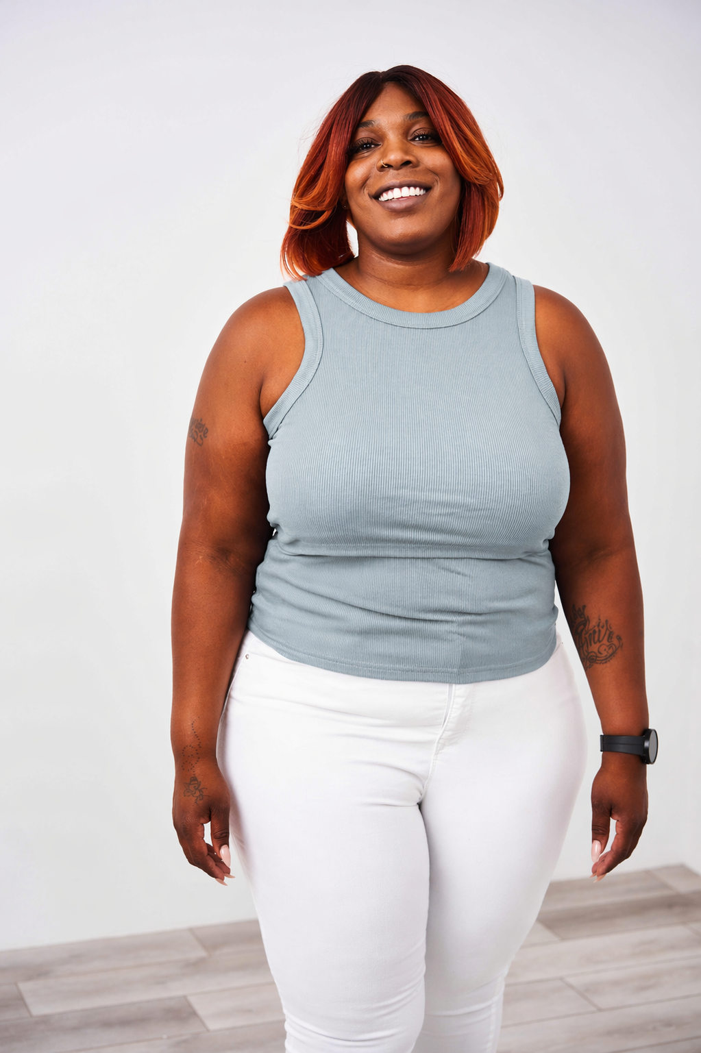 Woman wearing a light blue Latched Mama nursing tank top and white pants against a plain background.