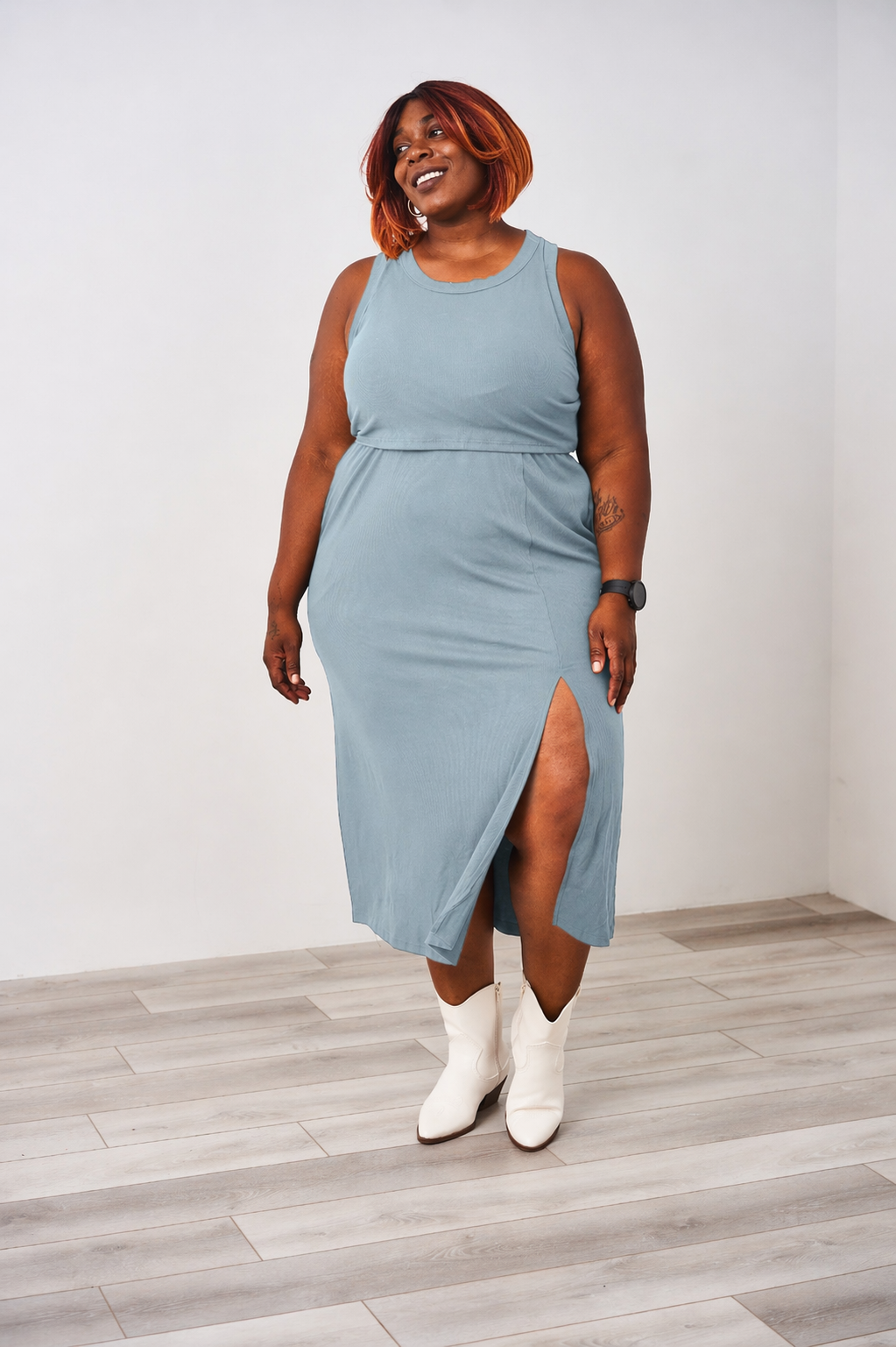 Woman wearing a dusty blue Latched Mama nursing ribbed midi dress with white boots.