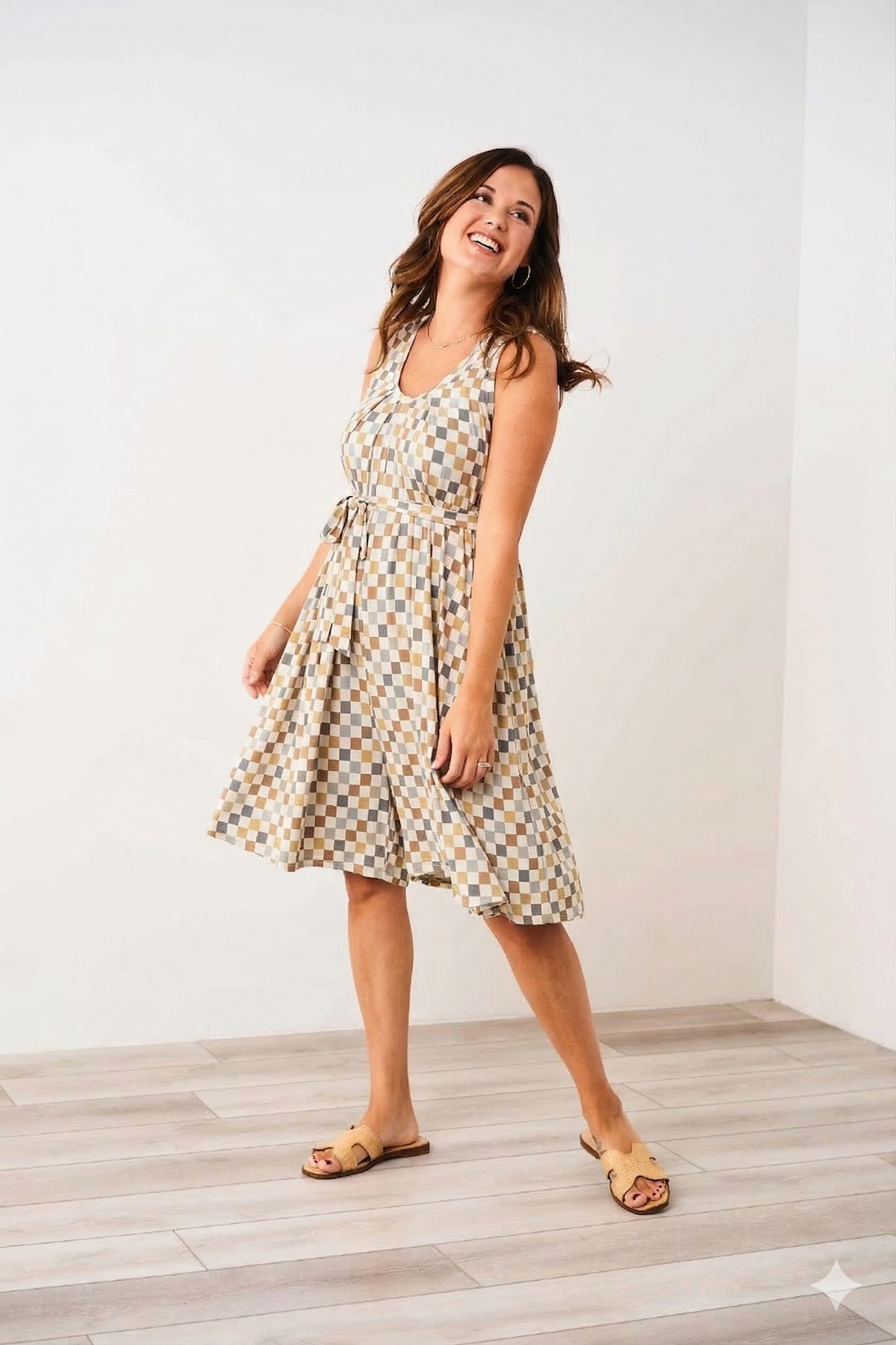 Woman wearing a checkered Latched Mama nursing romper standing in a room with white walls and wooden floor.