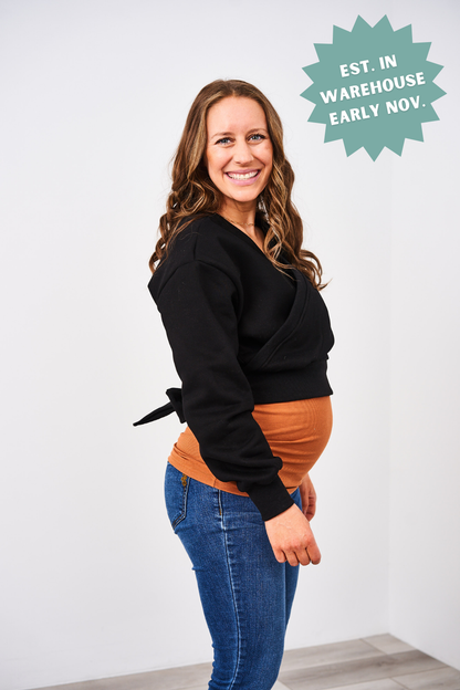 Woman wearing a black sweater over a brown top with text 'EST. IN WAREHOUSE EARLY NOV.'