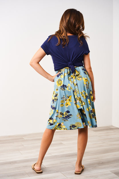 Woman wearing a Latched Mama blue nursing top on top of a Latched Mama floral nursing romper against a white wall.