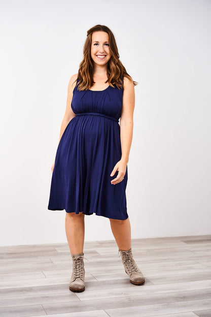 Woman standing and modeling a sleeveless Latched Mama Navy Momper® nursing romper with tie waist