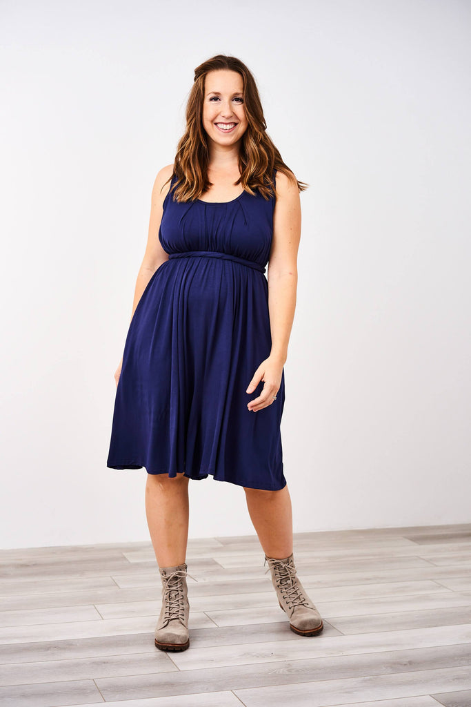 Woman standing and modeling a sleeveless Latched Mama Navy Momper® nursing romper with tie waist