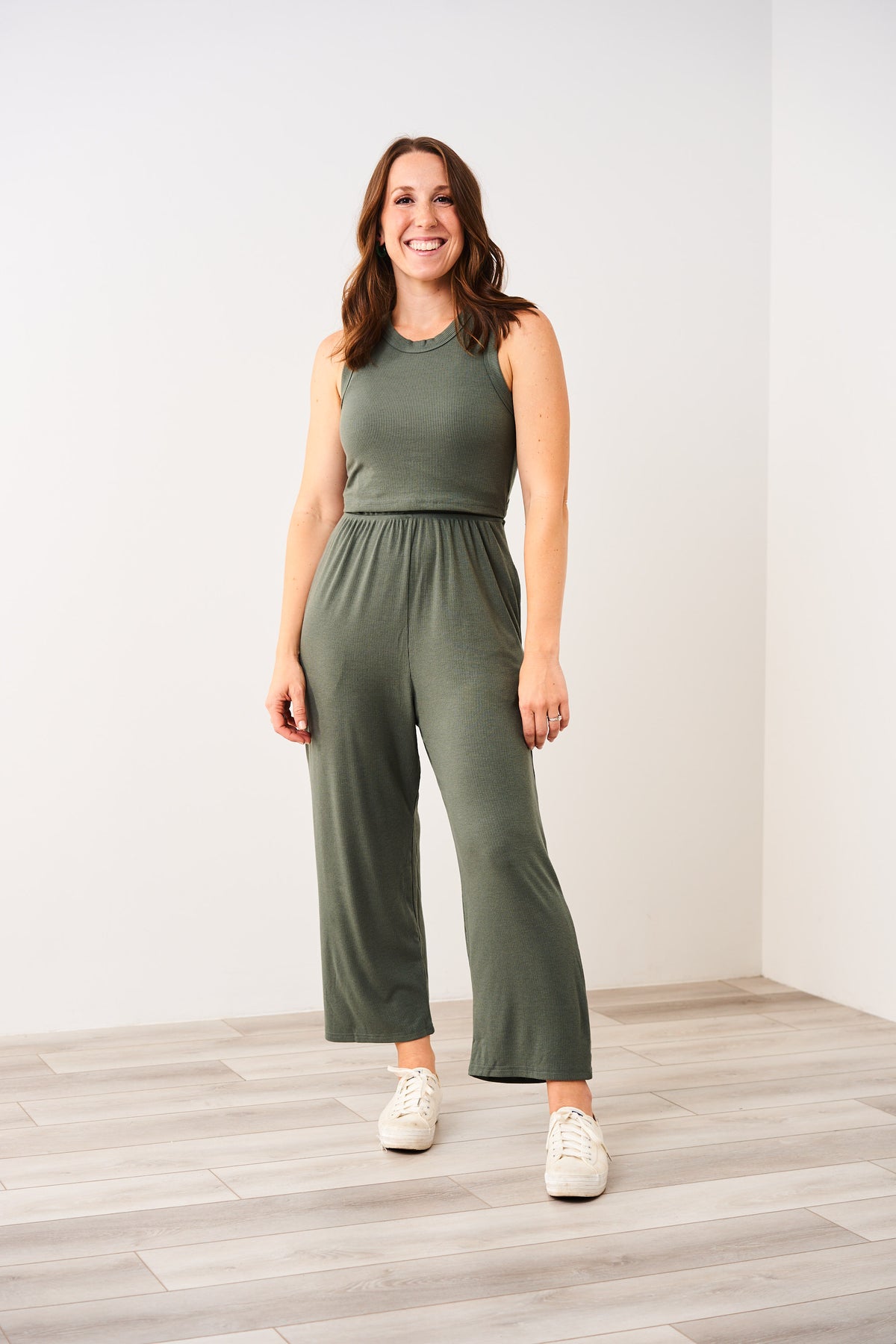 Woman wearing a green Latched Mama nursing jumpsuit standing against a white wall.