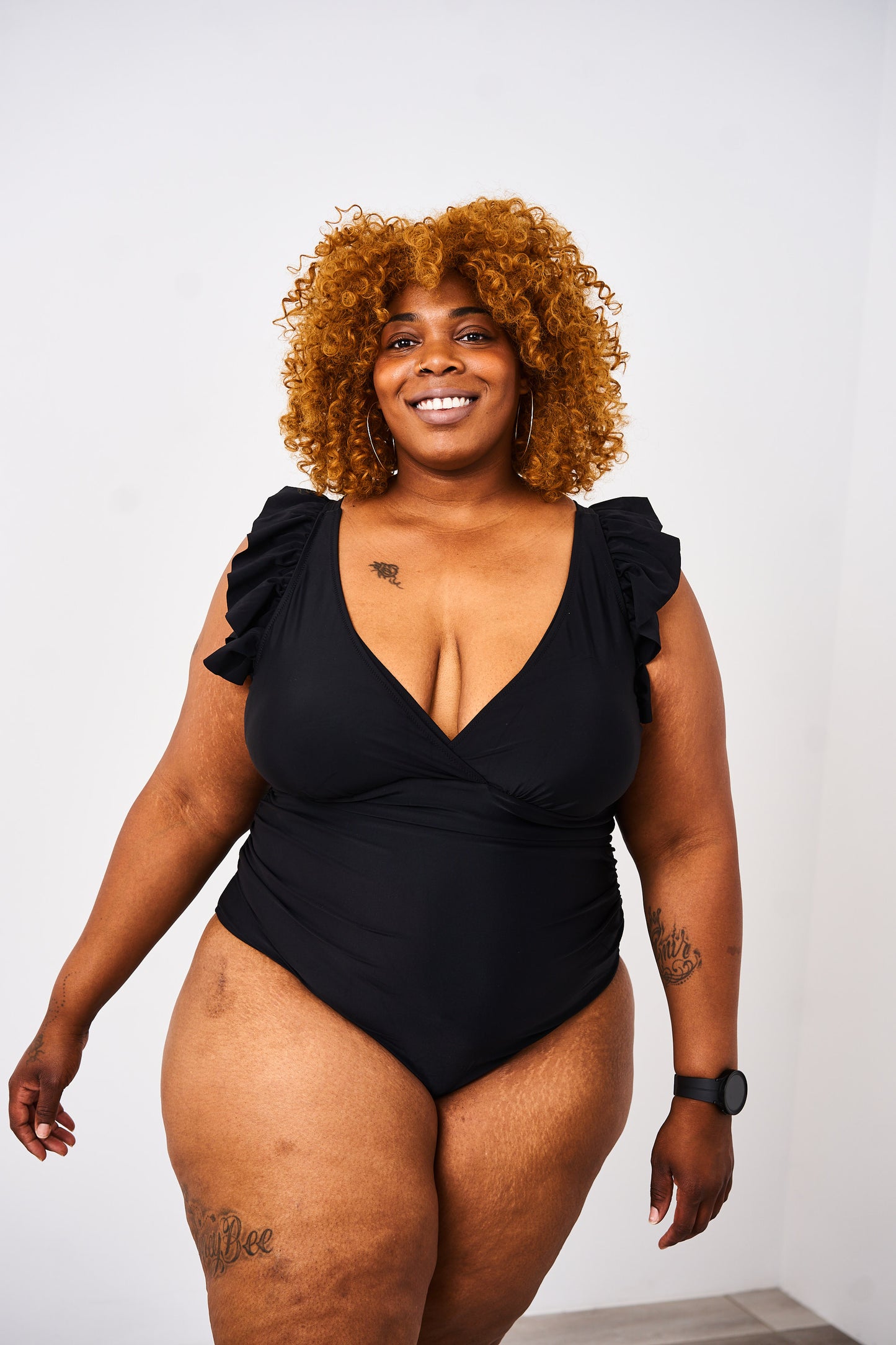 A woman wearing a Latched Mama lace-up nursing swim one-piece with ruffles on the shoulders and a v-neck design.