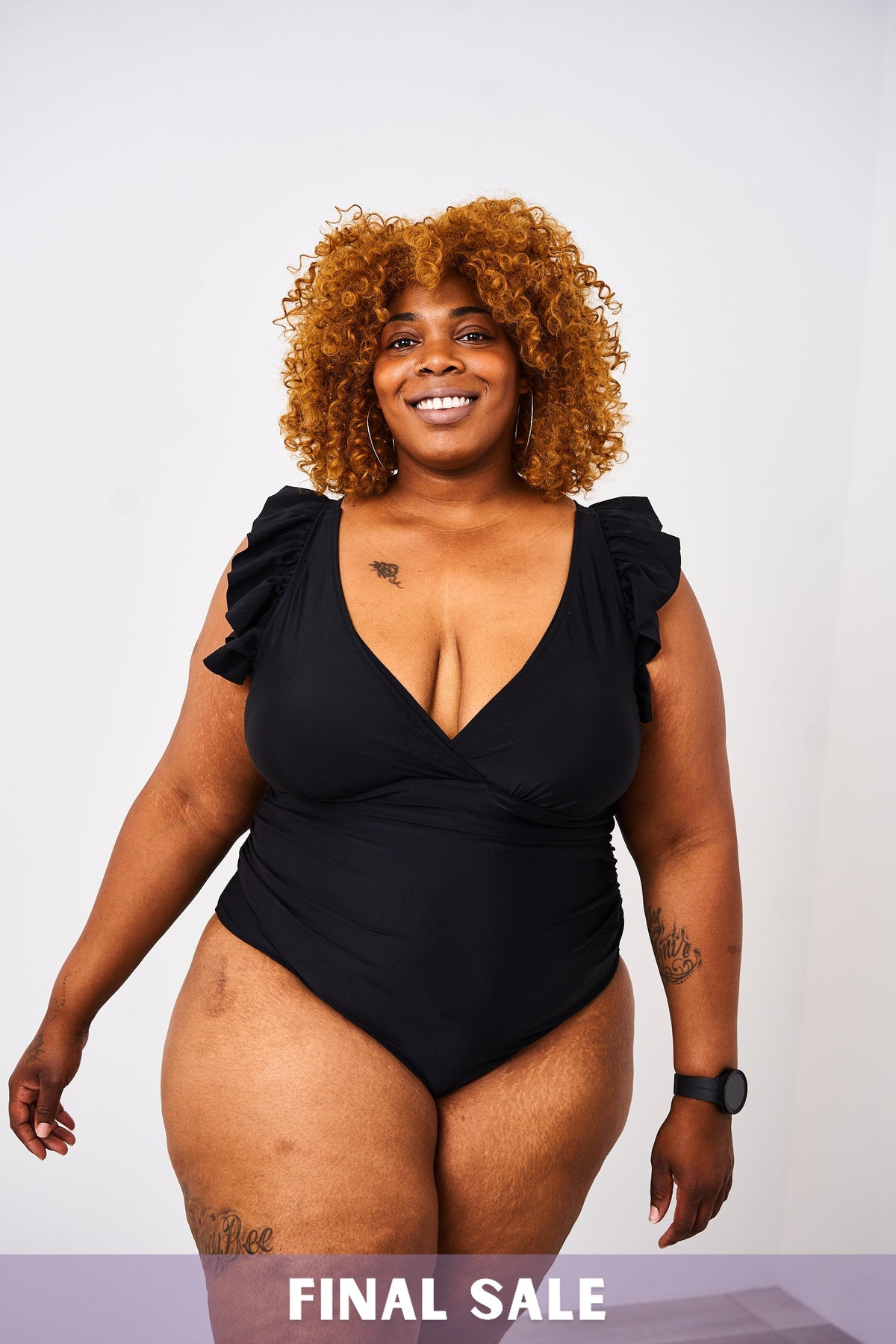 A woman wearing a Latched Mama lace-up nursing swim one-piece with ruffles on the shoulders and a v-neck design.