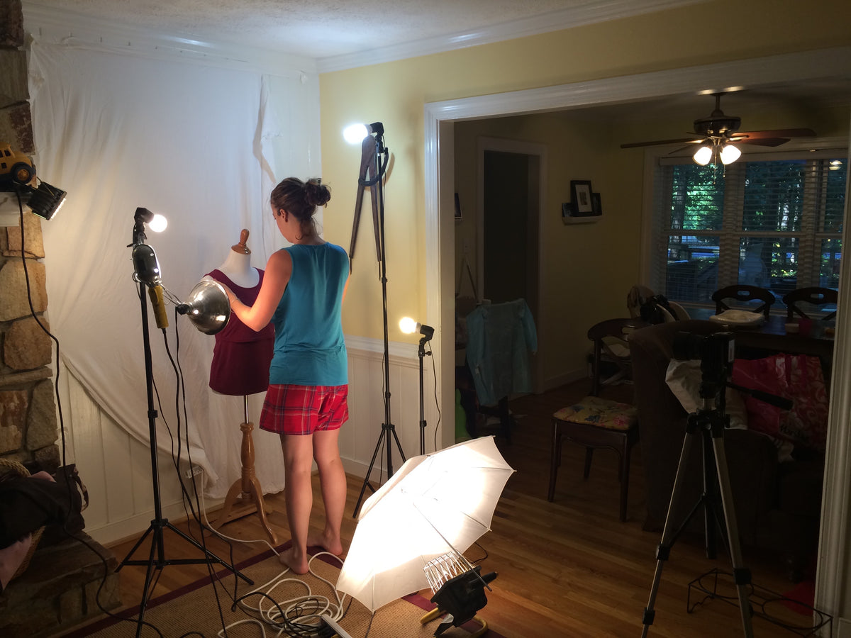 Early Latched Mama product photography setup at home, with a mannequin, white backdrop, and studio lights beside the dining room