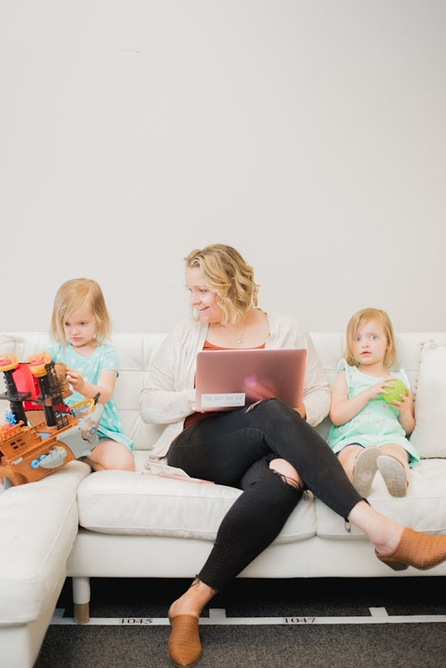 A Latched Mama mother working on her laptop with her two children beside her on a sofa